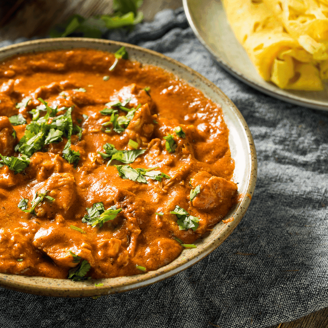 Bowl of creamy chicken tikka masala garnished with cilantro, served with Indian bread.