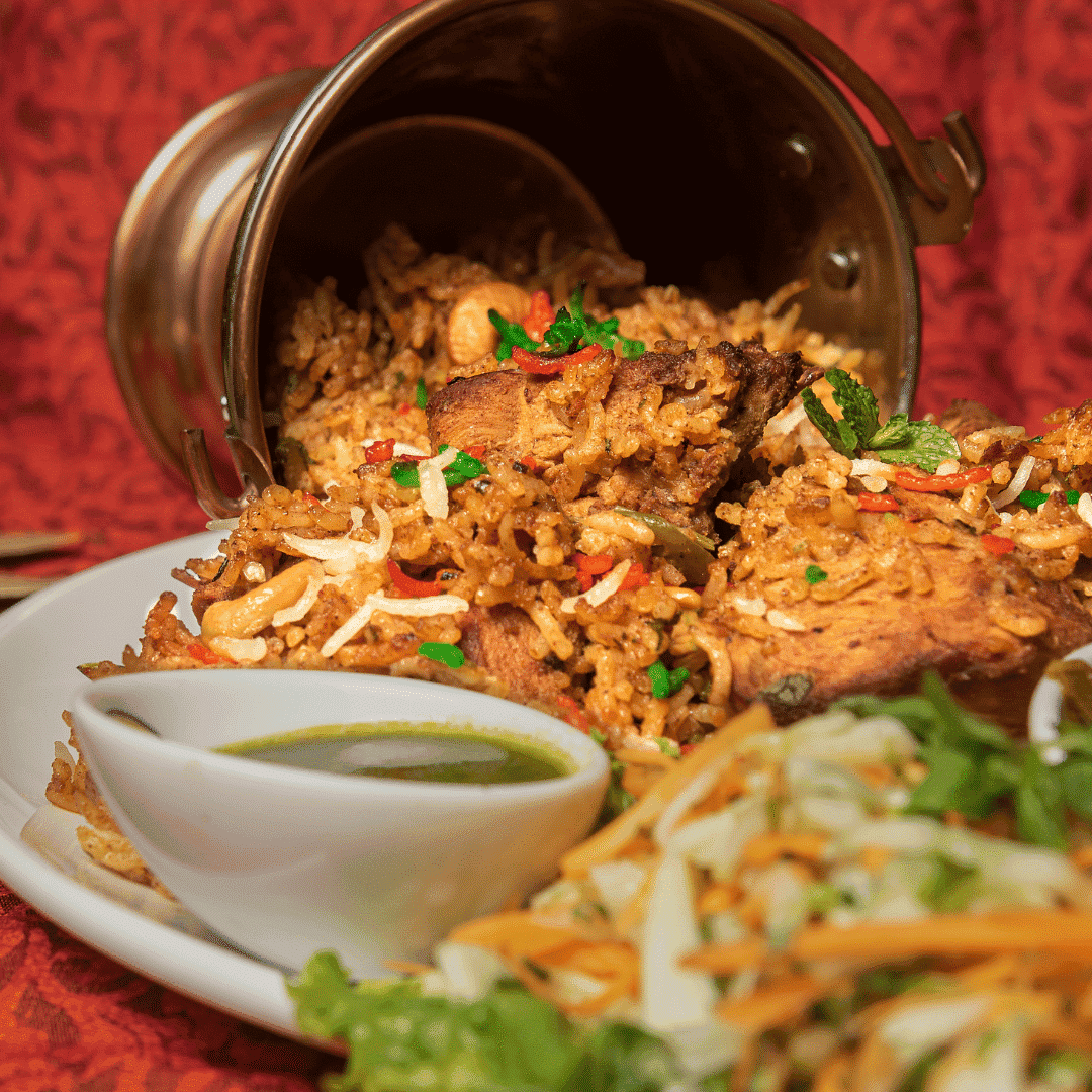 A plate of spicy biryani topped with herbs, next to a small bowl of green chutney.