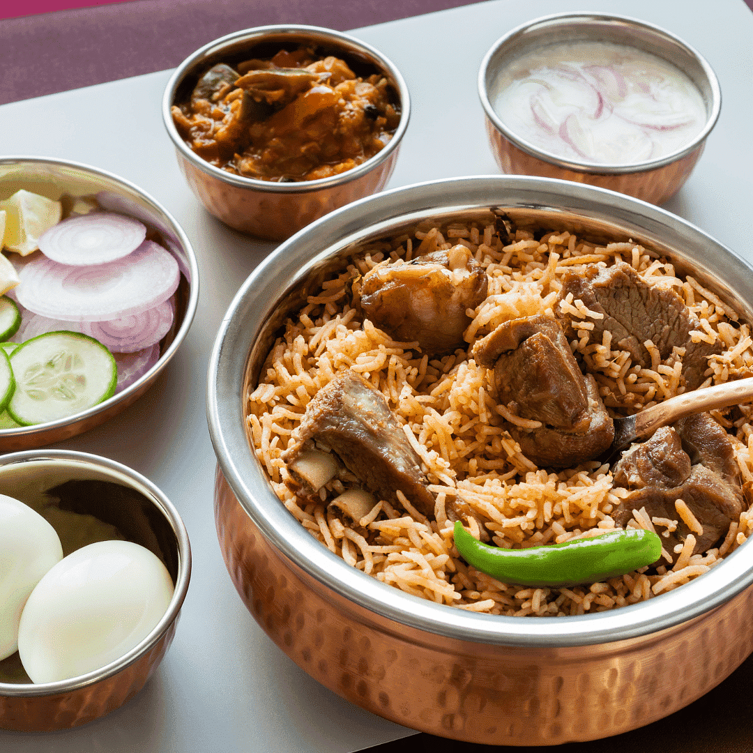 A plate of mutton biryani with boiled eggs, sliced vegetables, curry, and yogurt sauce in copper bowls.