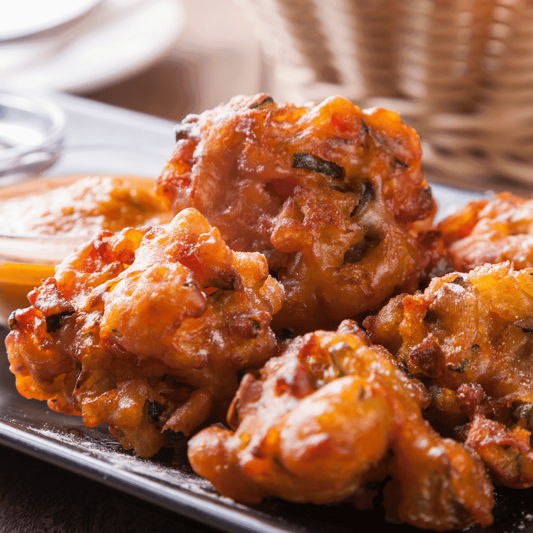 Close-up of crispy fritters on a plate with a dipping sauce in the background.