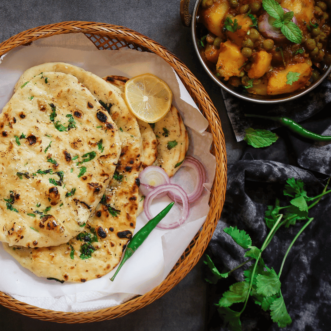 Basket of naan with sliced onions and chili, paired with a bowl of potato and pea curry.