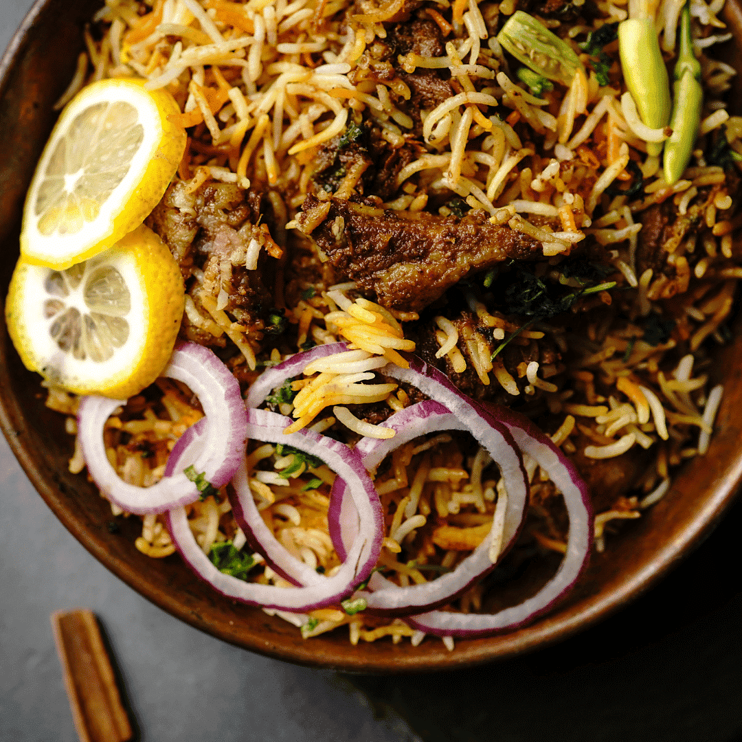 Plate of biryani with lemon slices, red onion rings, herbs, and a green chili pepper on top.