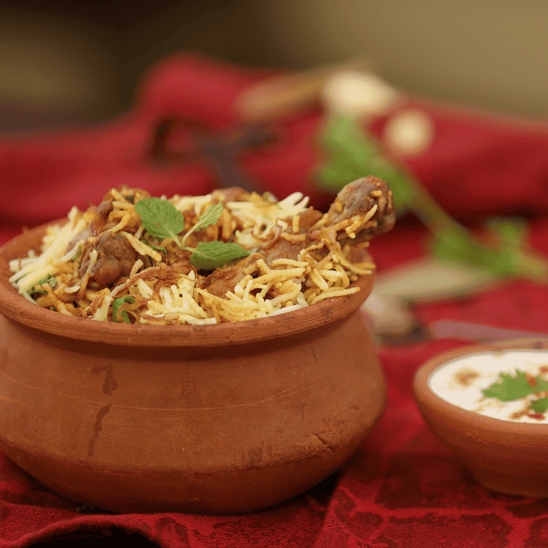 Clay pot filled with flavorful biryani garnished with herbs, placed on a red cloth with yogurt.